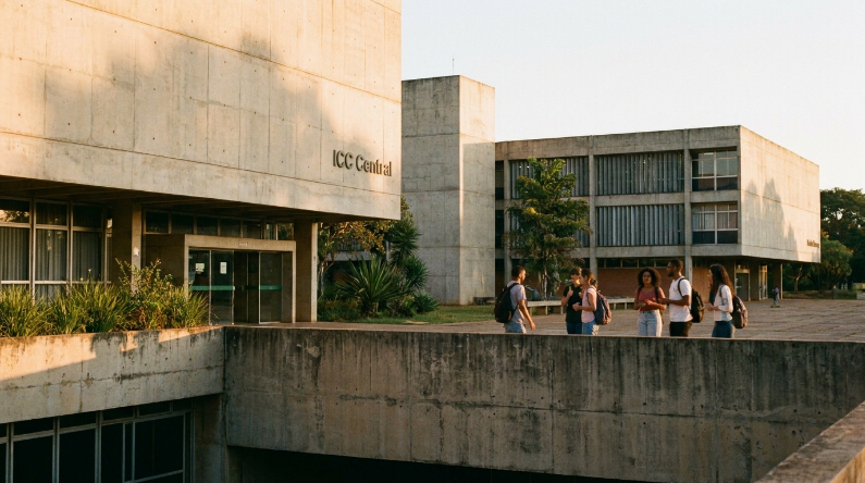 Um grupo de estudantes caminha em frente ao prédio do ICC Central, uma construção de arquitetura brutalista em concreto, durante o entardecer.